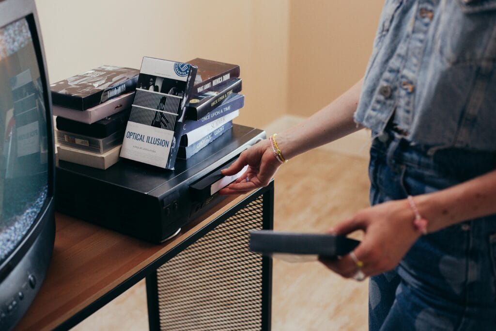 A person setting up a VCR with VHS tapes in a cozy indoor setting.
