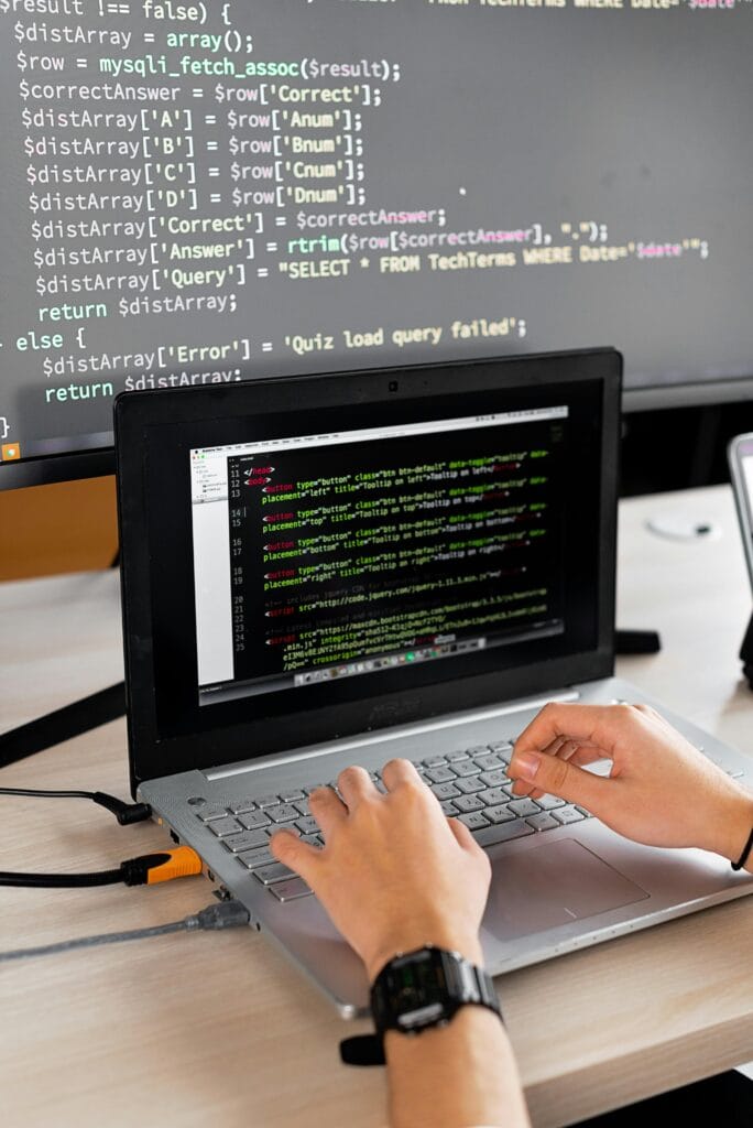 Person coding at a desk with laptop and external monitor showing programming code.